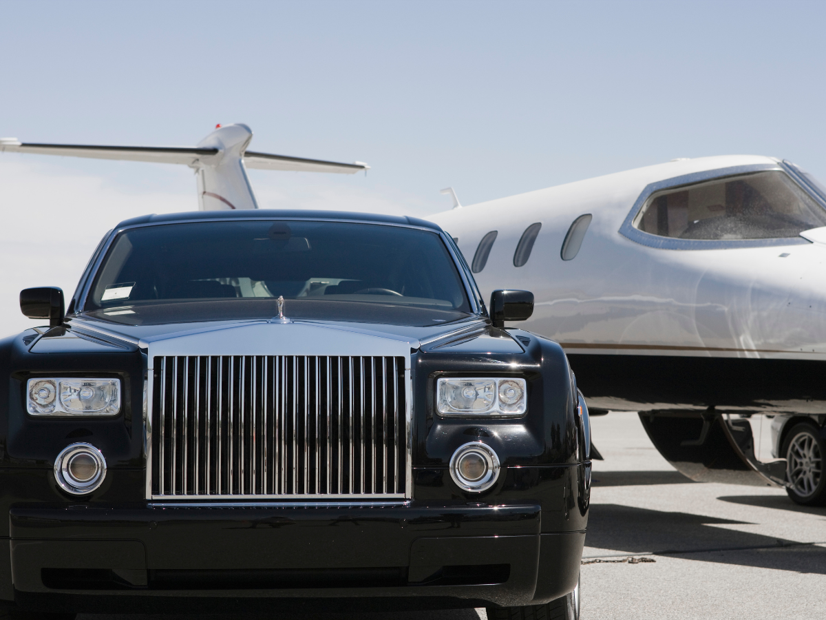 Black Rolls-Royce parked on tarmac in front of a white private jet on a sunny day.