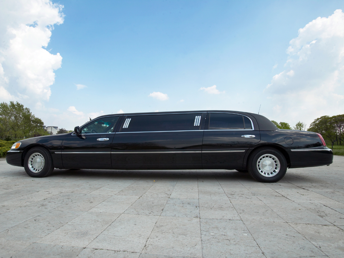 Black limousine parked on a paved surface, blue sky with clouds in the background.