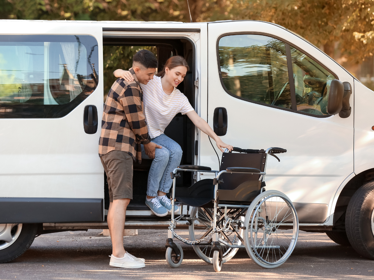 Man assisting a person from a van, wheelchair nearby.