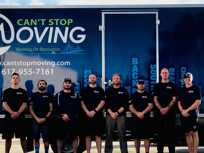 Group of movers in front of a blue moving truck with company logo and city skyline.