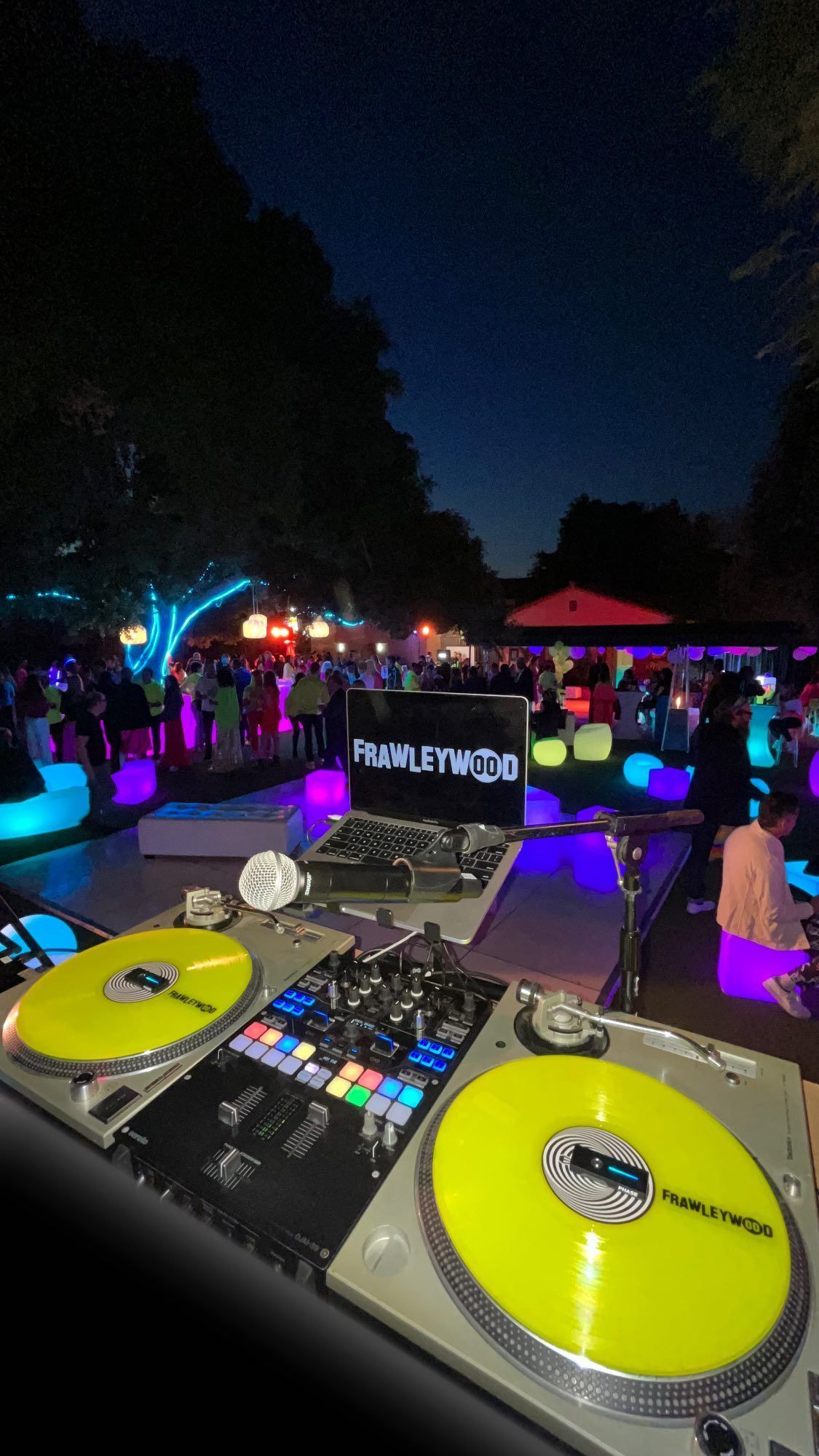 A dj is playing music at a party with a crowd in the background.