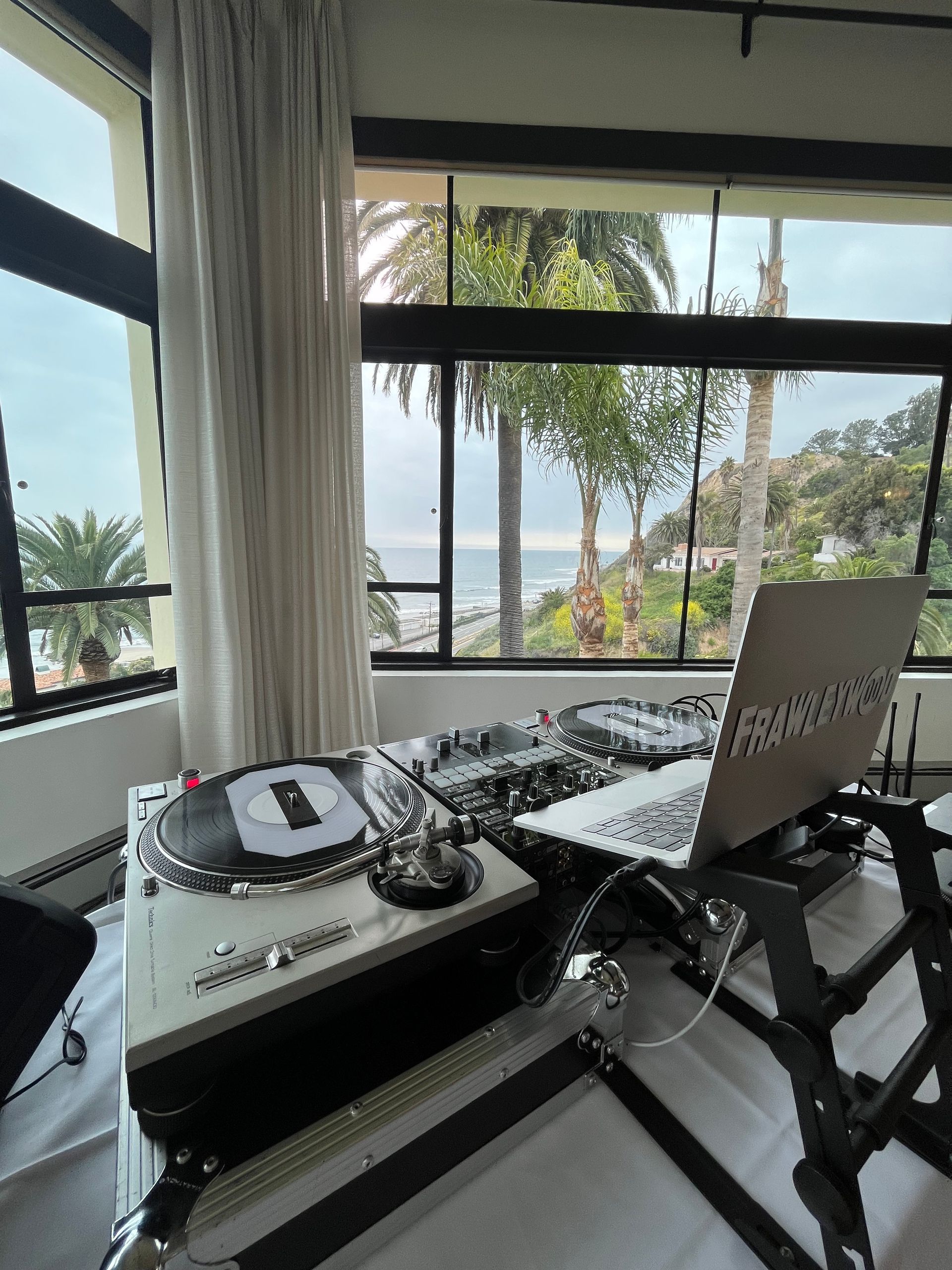 A laptop is sitting on a table next to a turntable in a room with a view of the ocean.