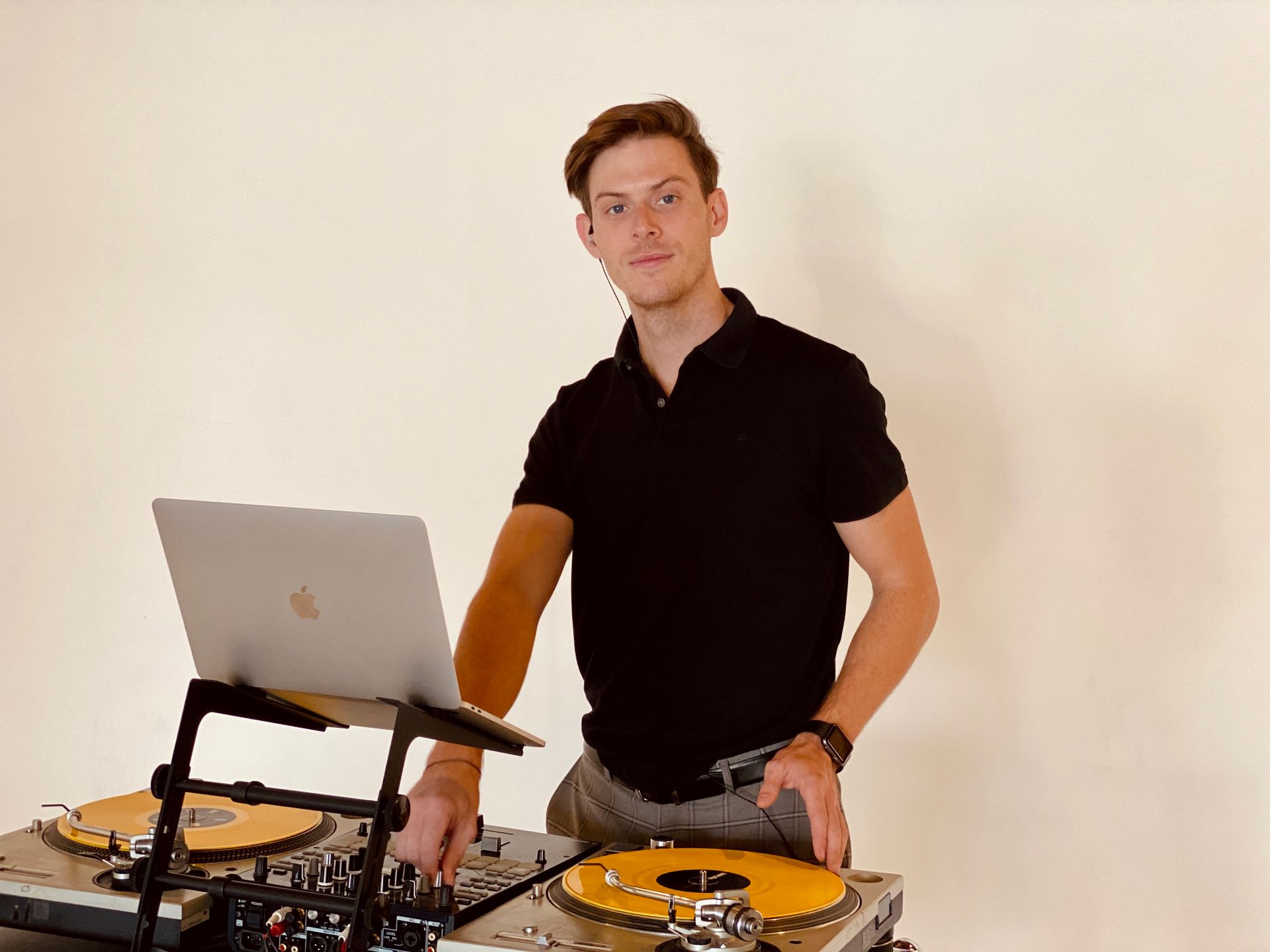 A young man is standing in front of a laptop and a turntable.