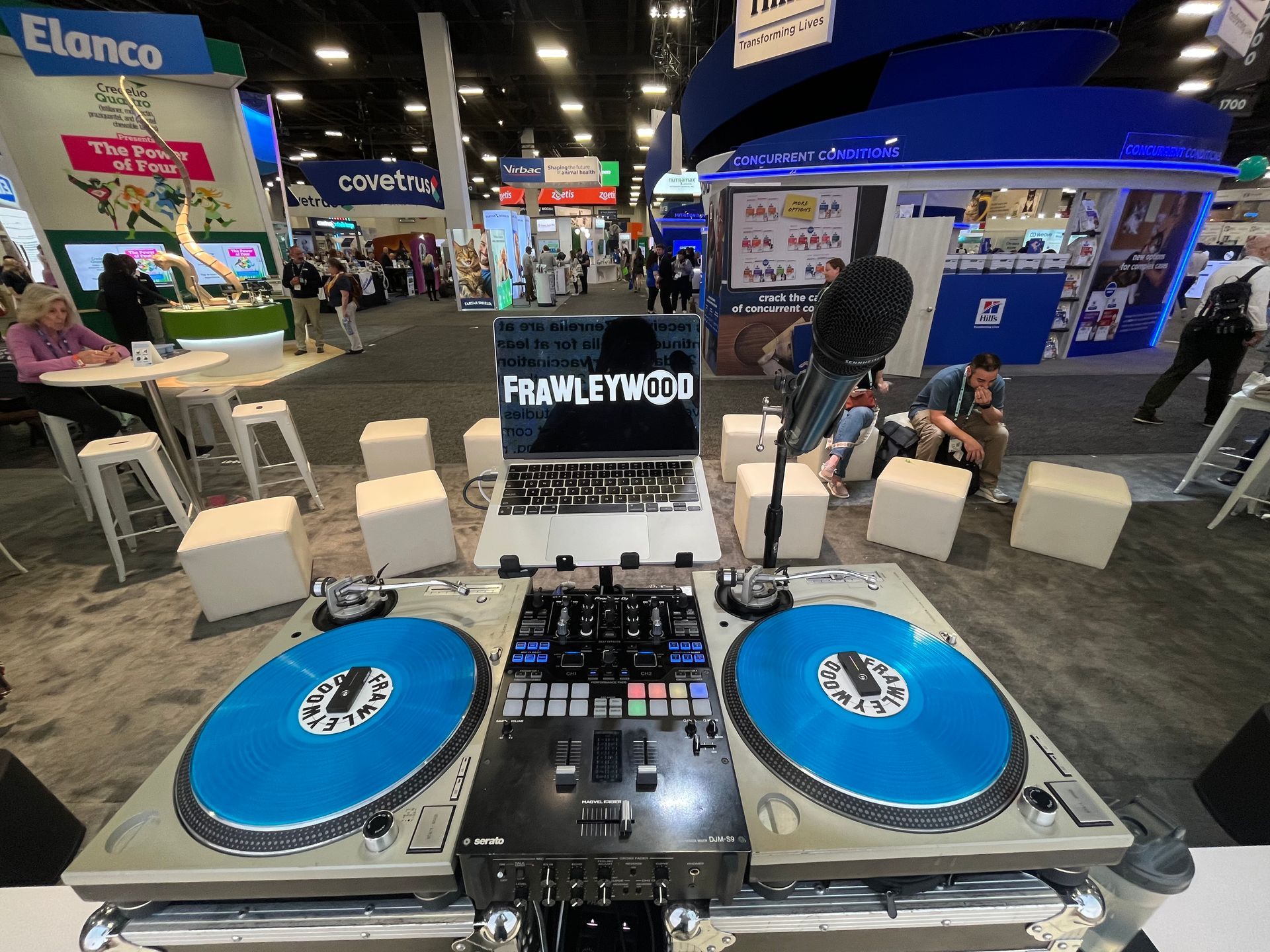 A dj booth at a convention with two turntables and a laptop.