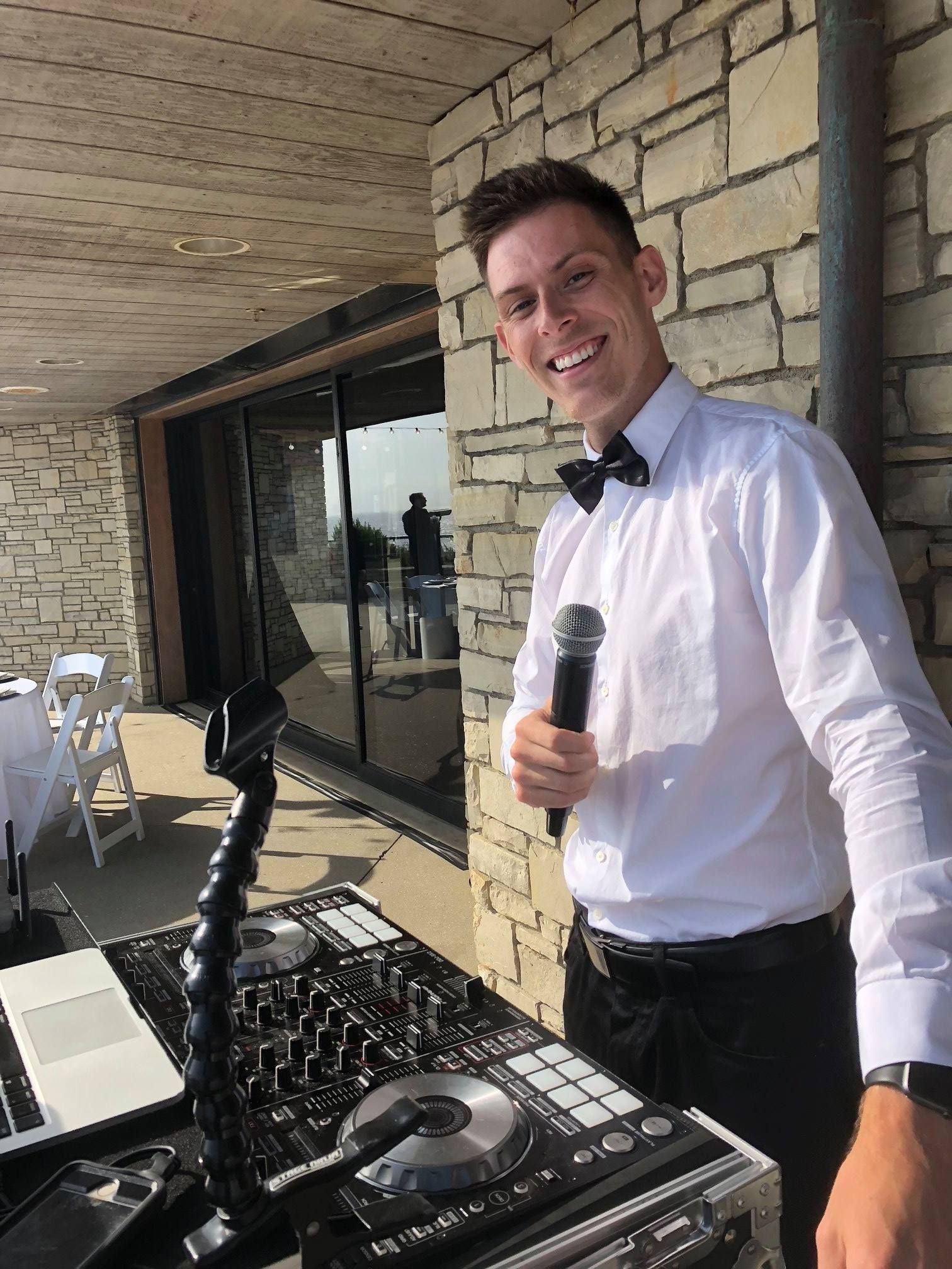 A man in a bow tie is holding a microphone in front of a dj mixer.