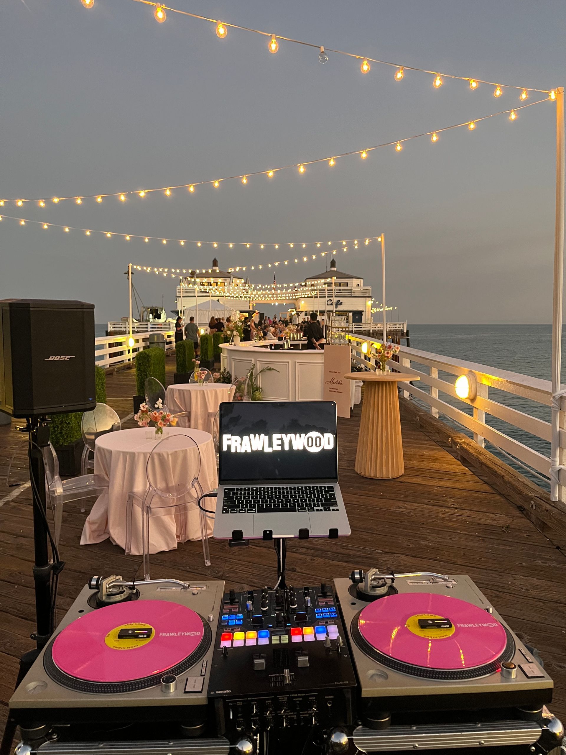 A laptop is sitting on top of two turntables on a pier.