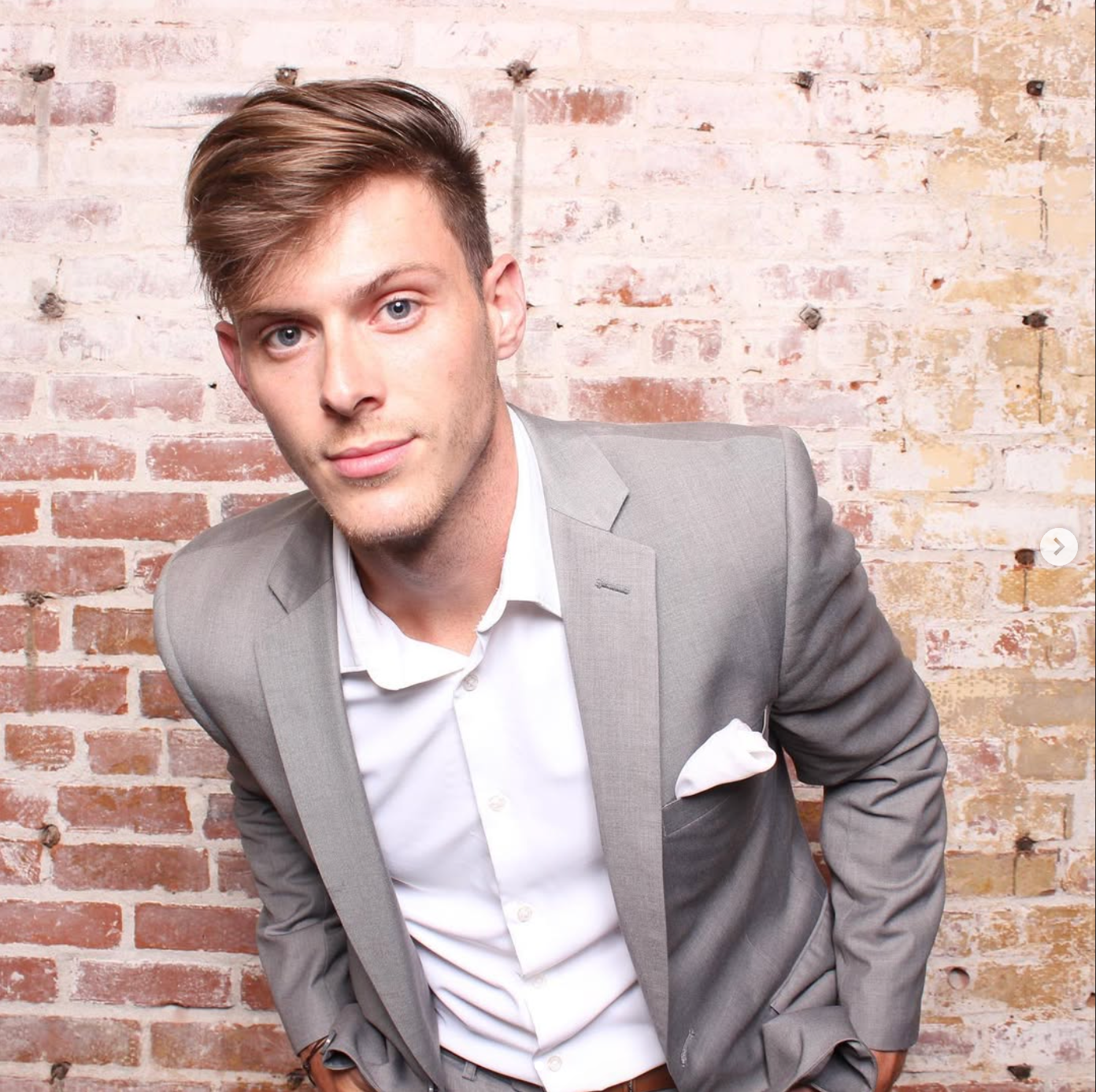 A man in a suit is standing in front of a brick wall