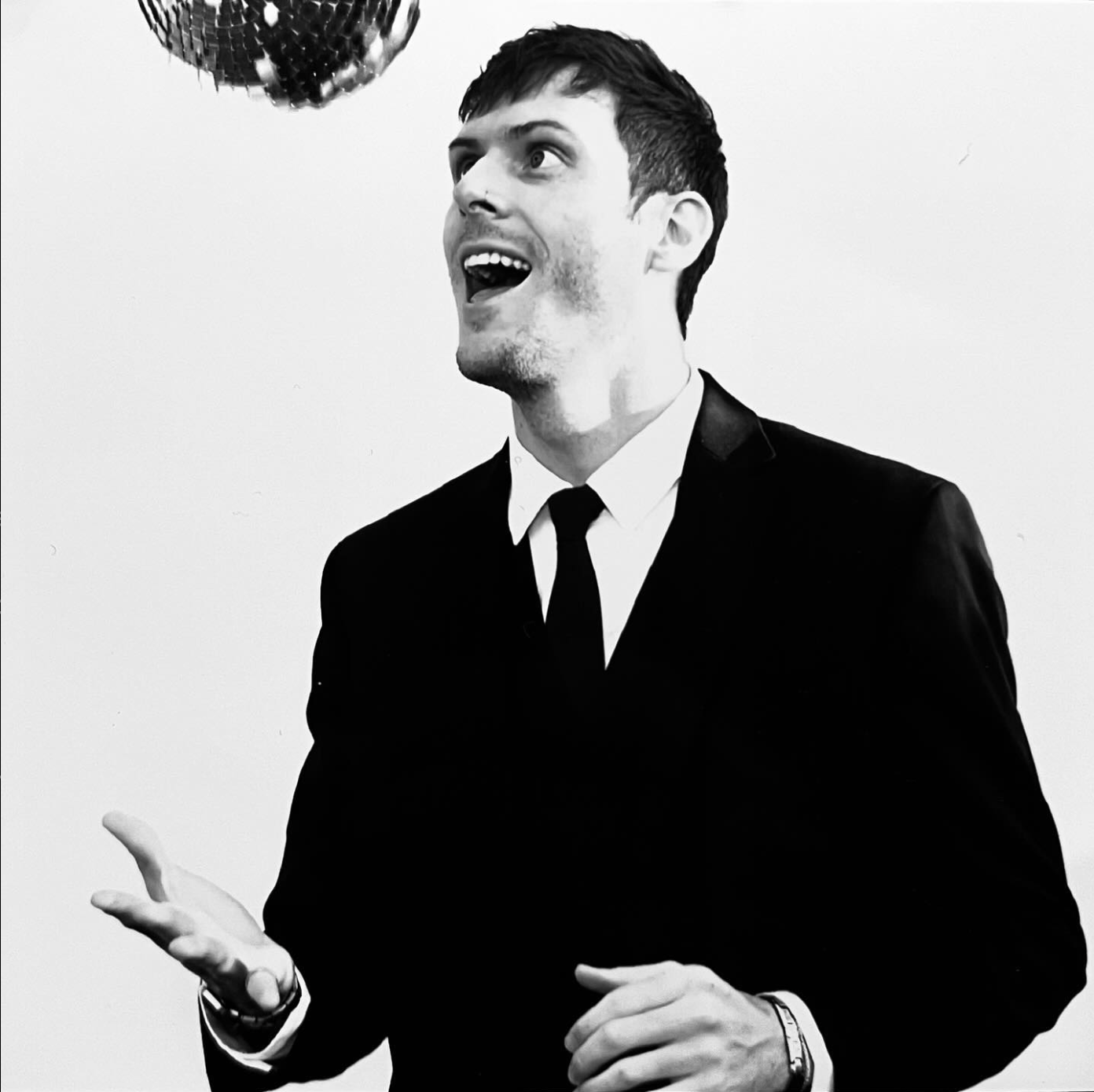 A man in a suit and tie is throwing a disco ball in the air