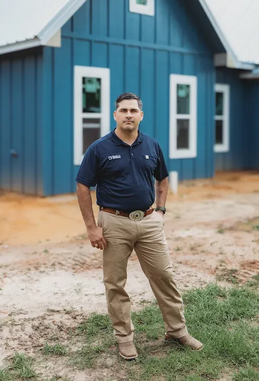 Man in polo shirt and khakis stands in front of a blue house under construction.