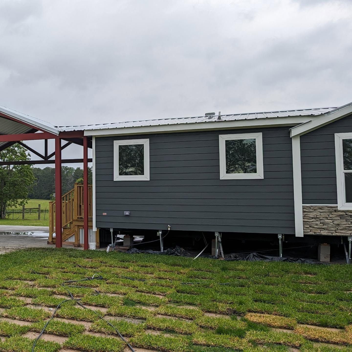 Dark gray house with white trim, elevated, and a red metal awning.
