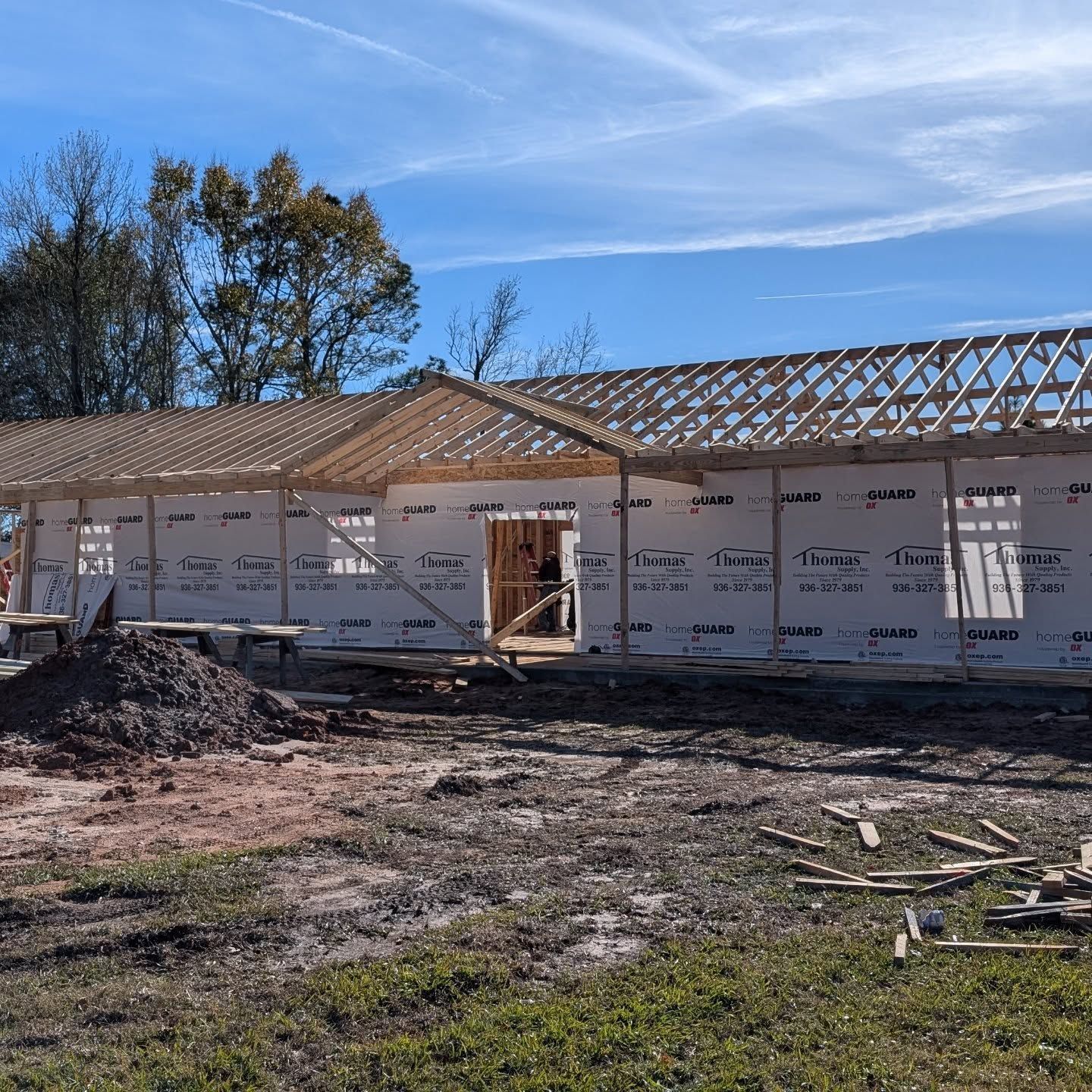 Construction site: wood frame building with roof trusses under a blue sky.