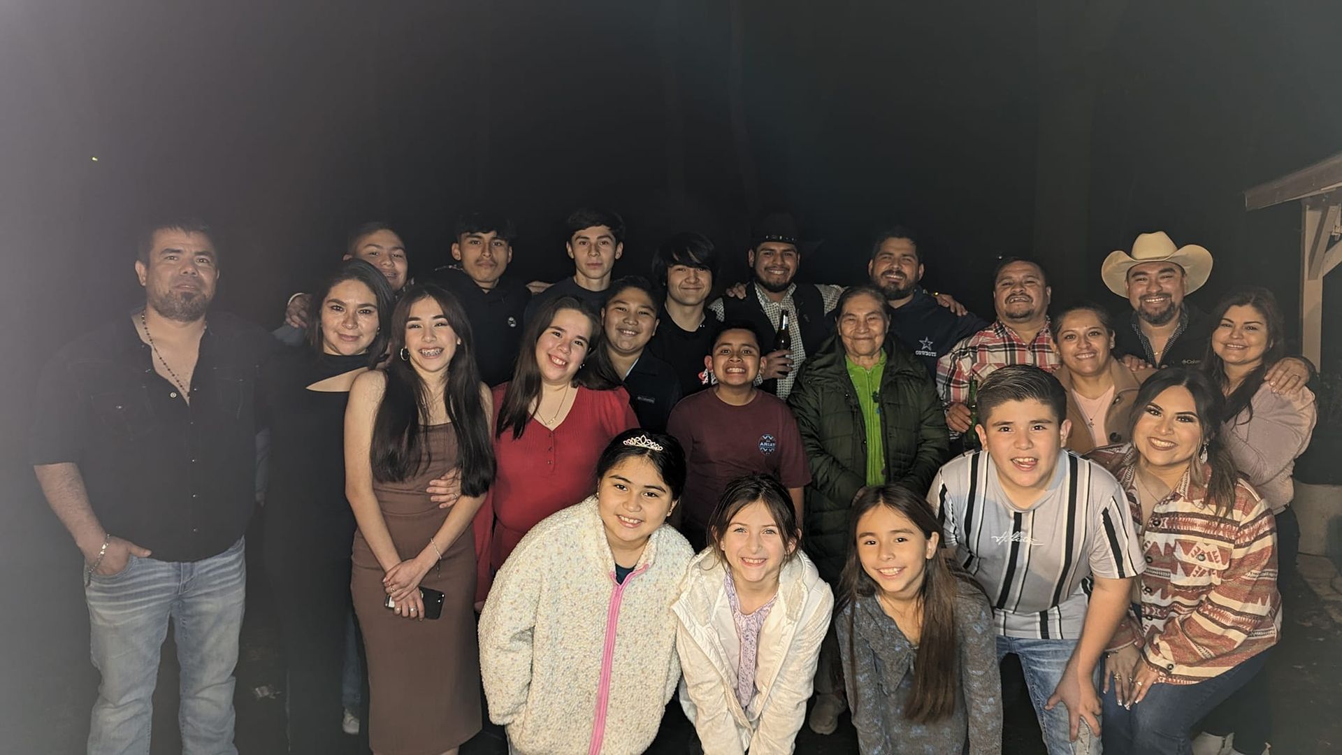 Group photo, smiling people outdoors at night.  Dark background. Many wearing sweaters, jackets.