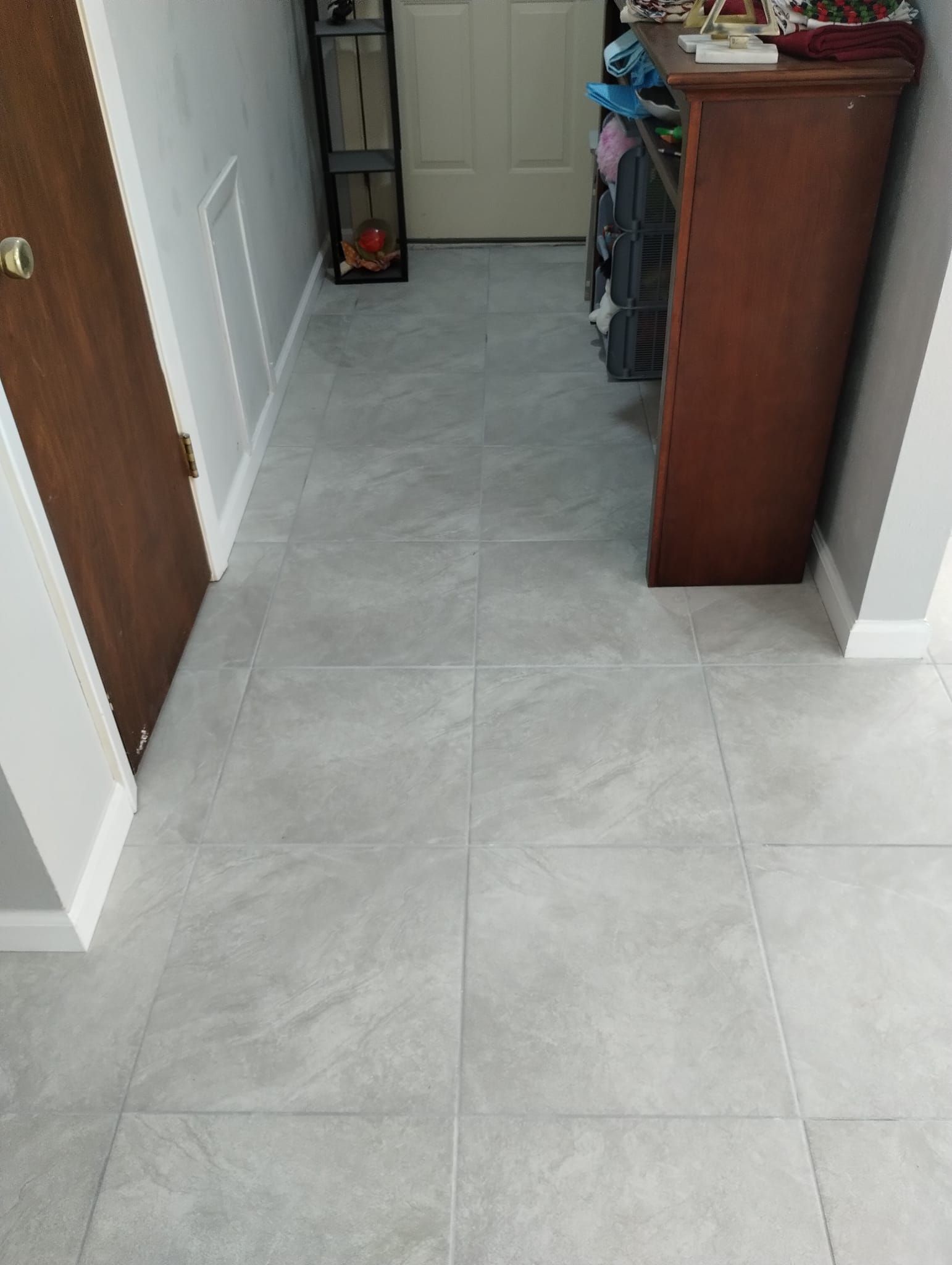 Gray tile floor in a hallway with a brown door, cabinet, and white trim.
