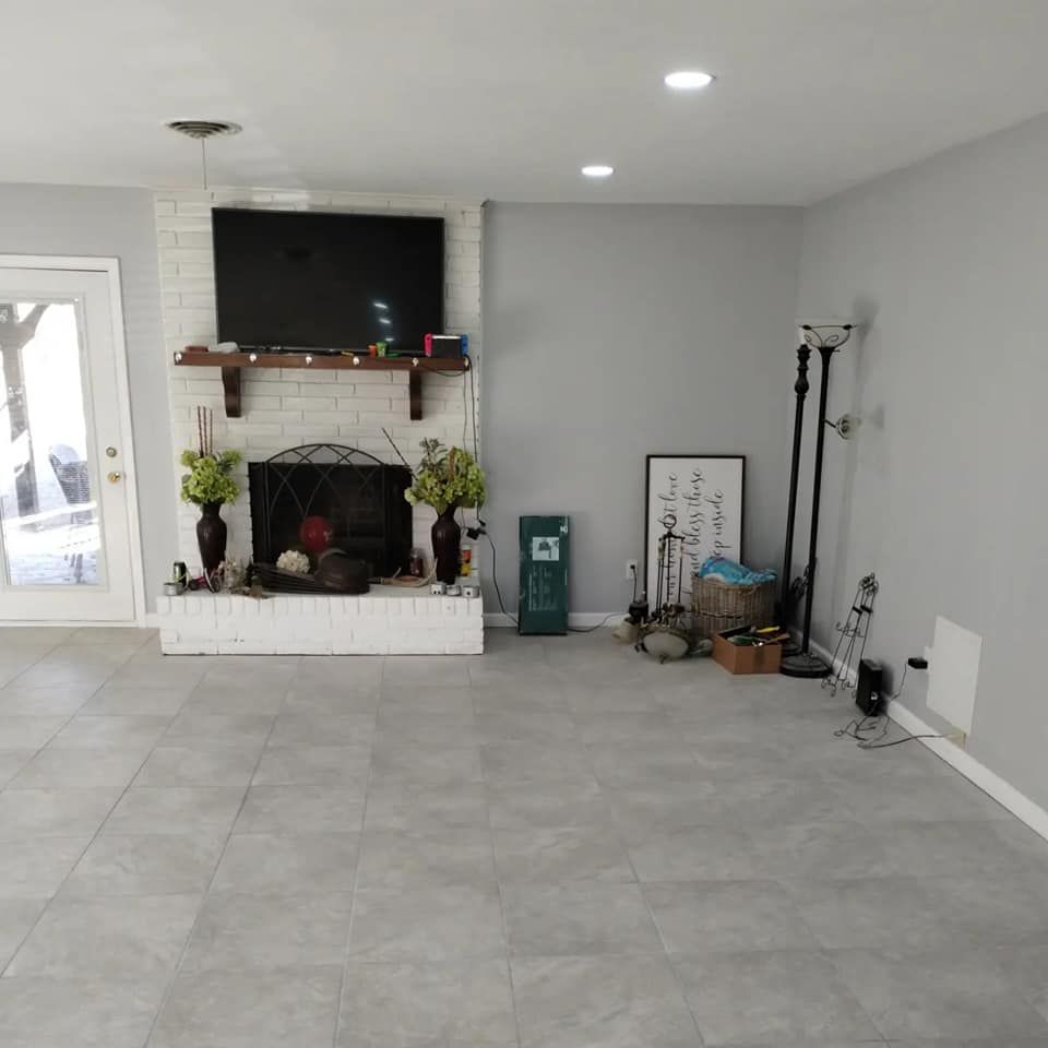 Empty living room with fireplace and mounted TV. Gray tile floors, white brick fireplace, gray walls.
