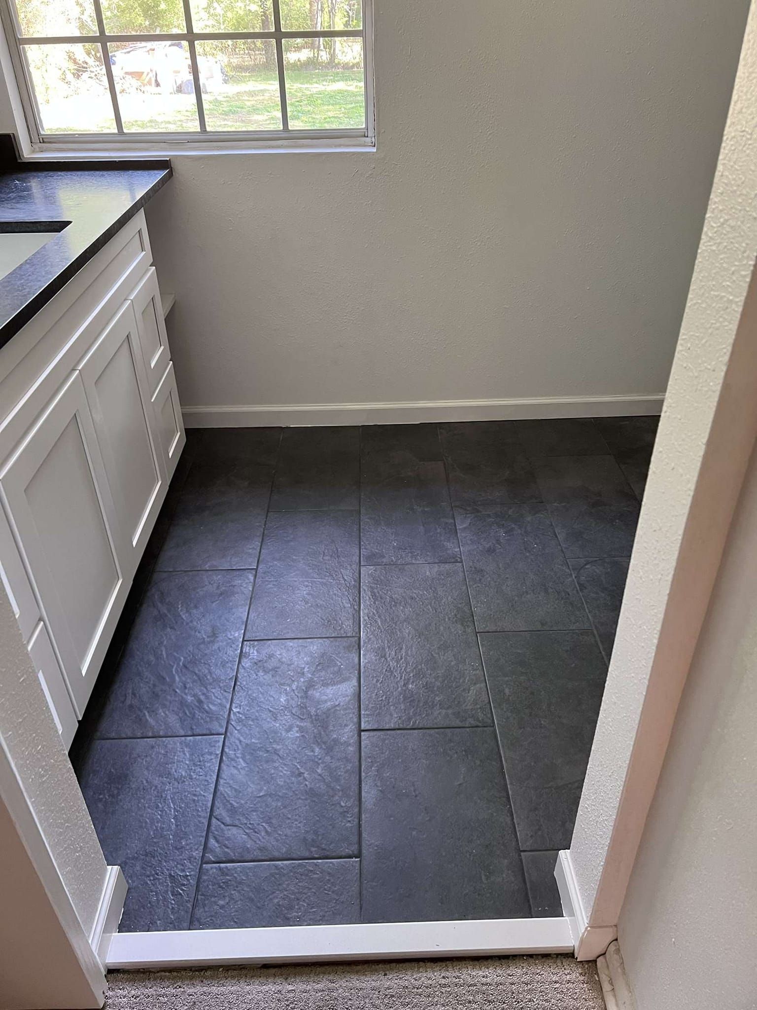 Small room with dark tiled floor, white cabinets, and a window.