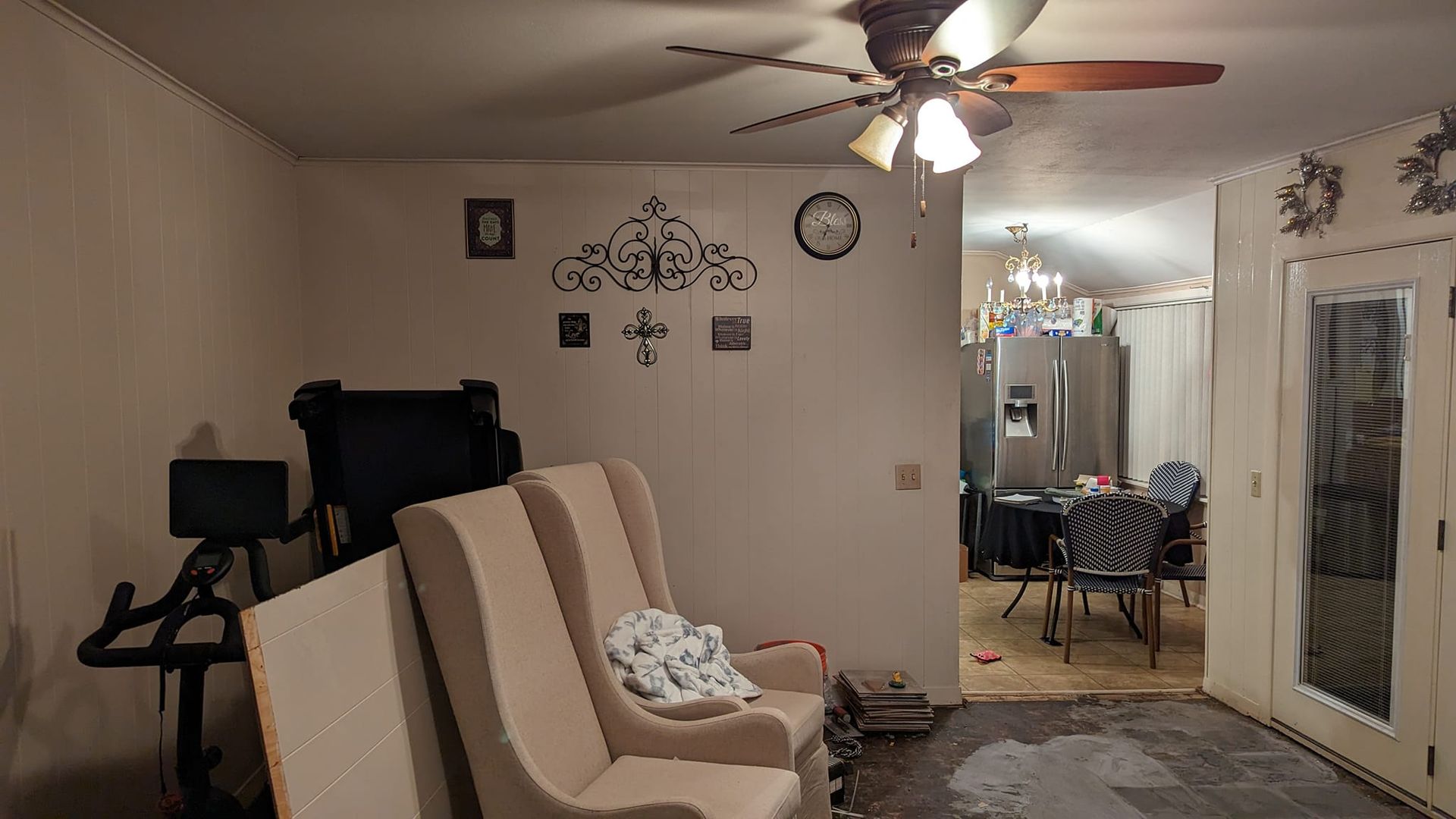 A living room with a cream-colored couch, a stationary bike, and an open doorway to a dining room.