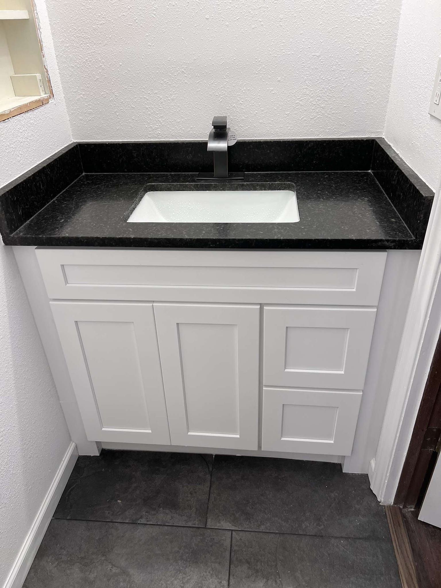 Bathroom vanity with black countertop and white cabinet, black faucet, and white sink.