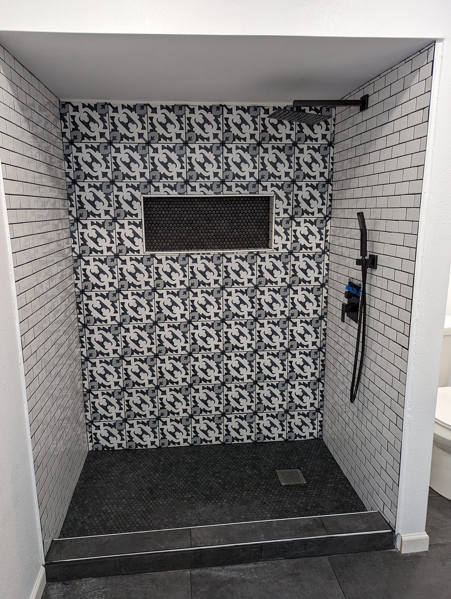 Shower stall with black and white patterned tile and a black floor.