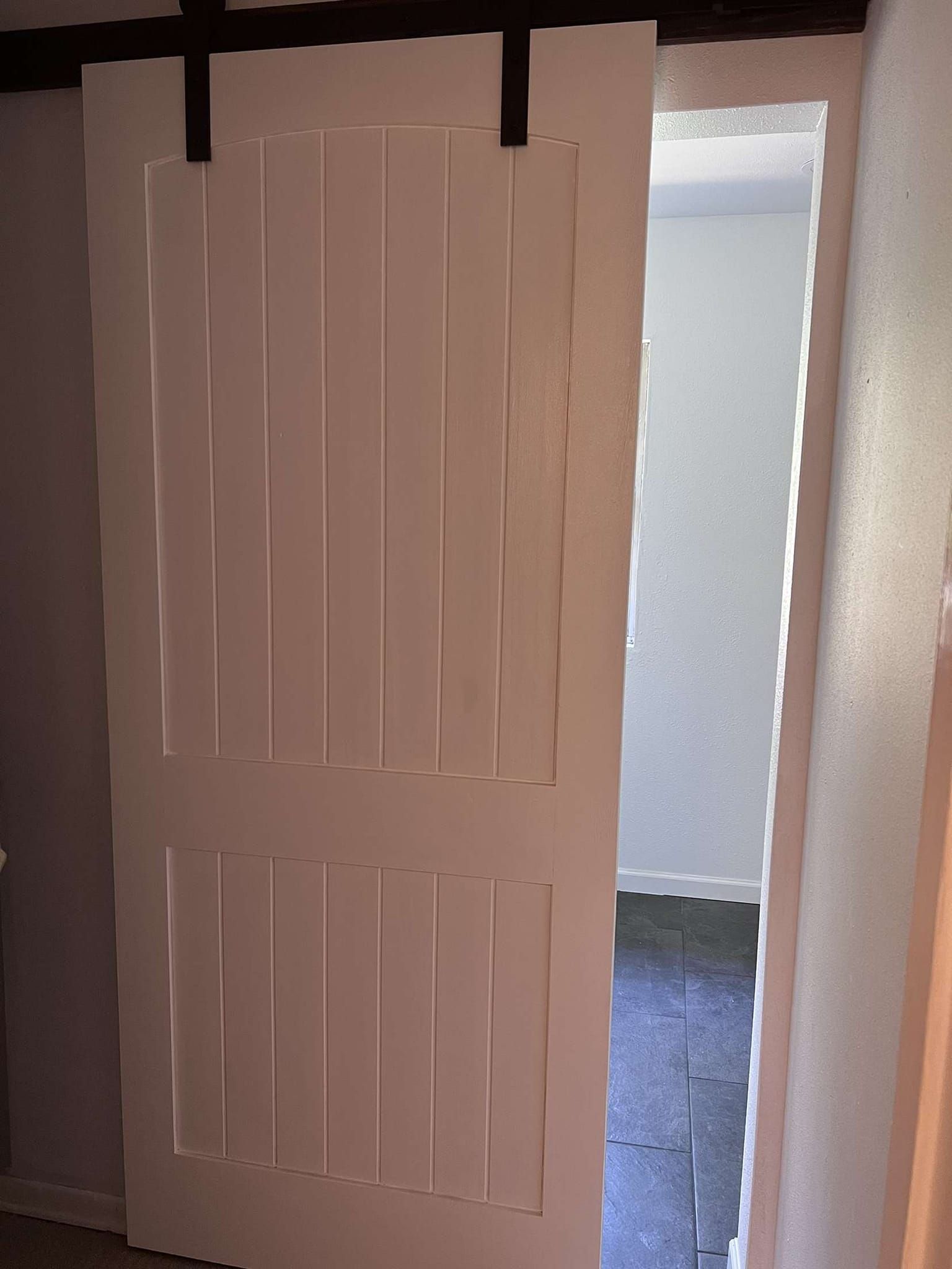 White barn door partially open, revealing a room with gray walls and dark flooring.