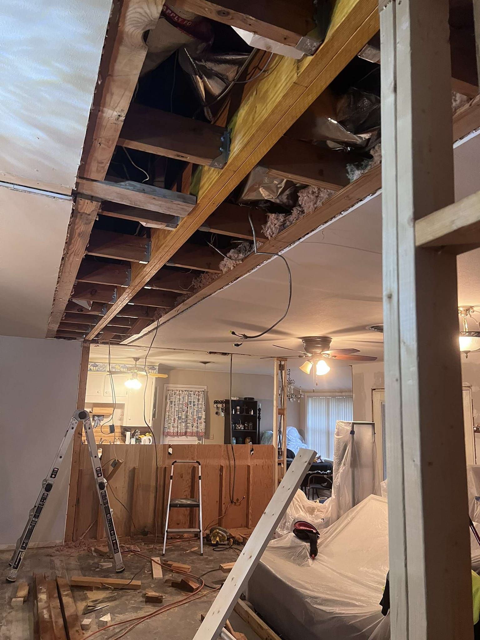 Interior during renovation; open ceiling exposing beams, insulation, and wiring; debris on floor.