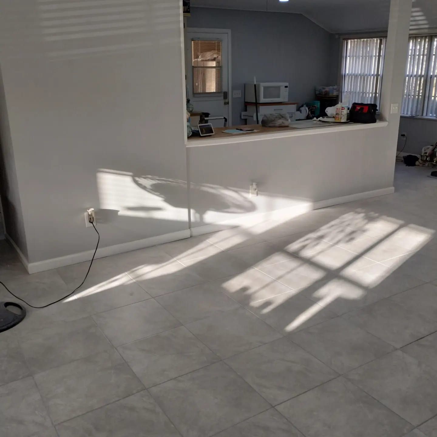 Sunlit interior with tile floor, partial wall, and kitchen area visible in the background.
