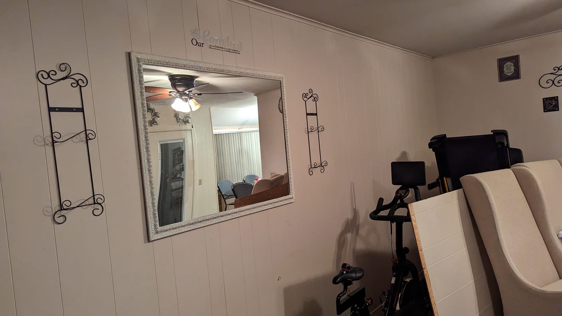 A room with a mirror reflecting another room, with decorative wall accents and a stationary bike.