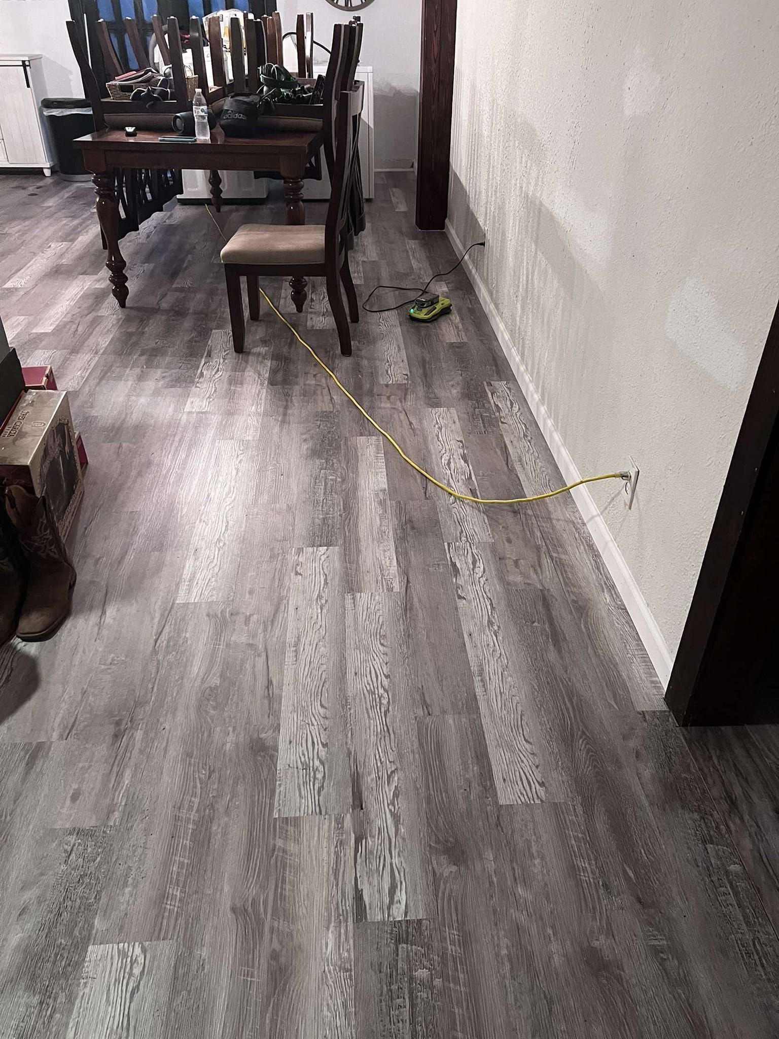 Gray wood-look flooring with a measuring tape extended along a wall near a door. A dining table and chairs are in the background.