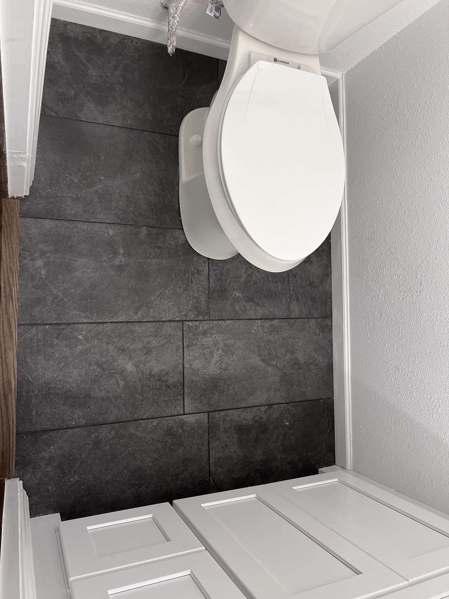 Bathroom with white toilet on dark gray tiled floor, white cabinets.