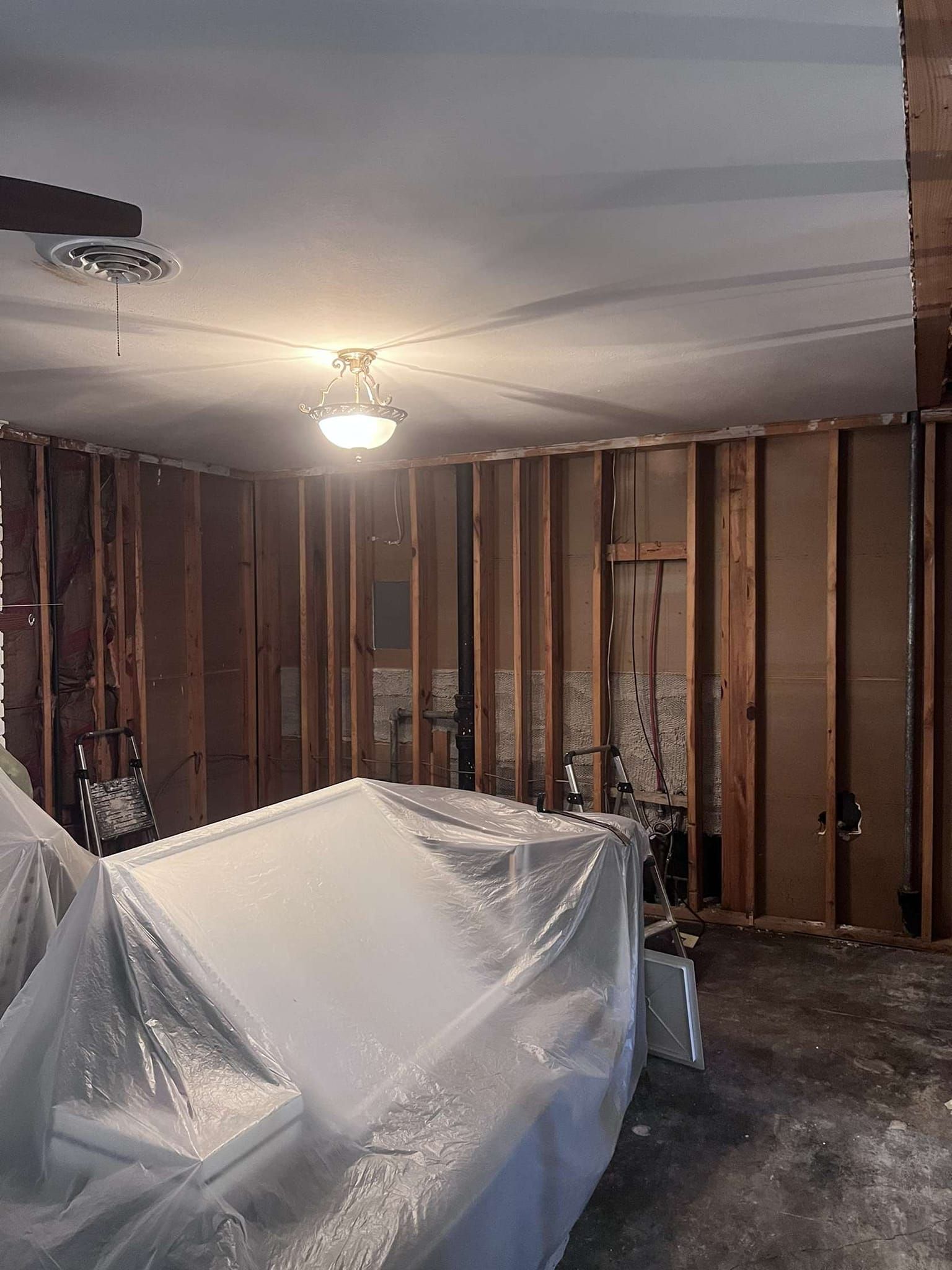 Interior of a room undergoing renovation, exposed wood framing, covered object, and damaged walls.