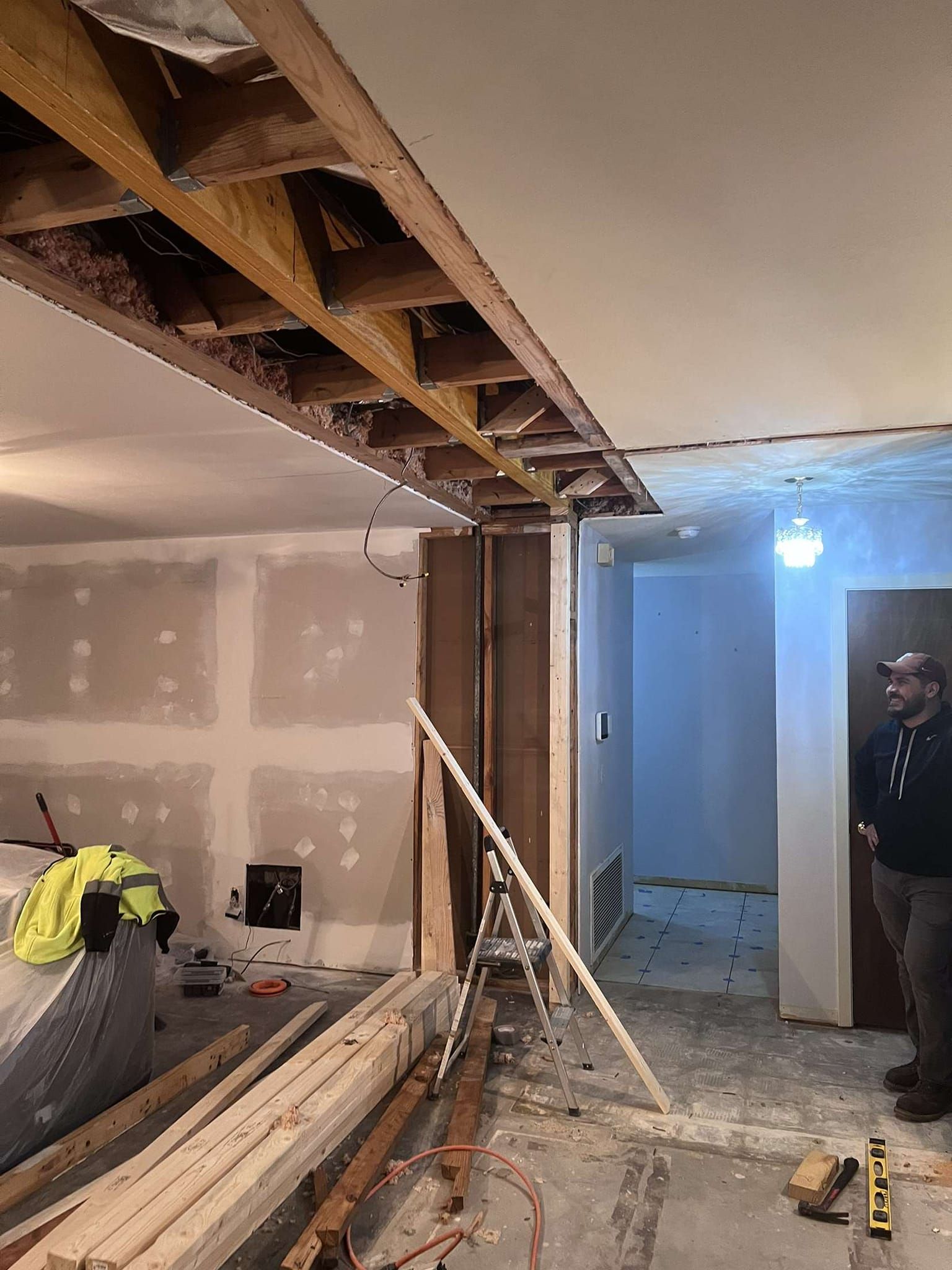 Interior renovation: Exposed ceiling beams, drywall, wood debris, person standing in doorway.