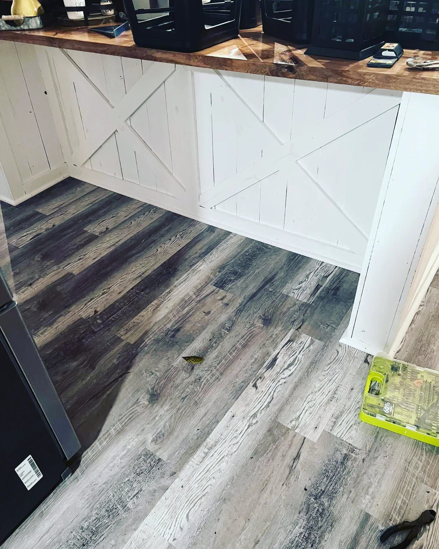 White kitchen island with X-shaped paneling and grey wood-look flooring.