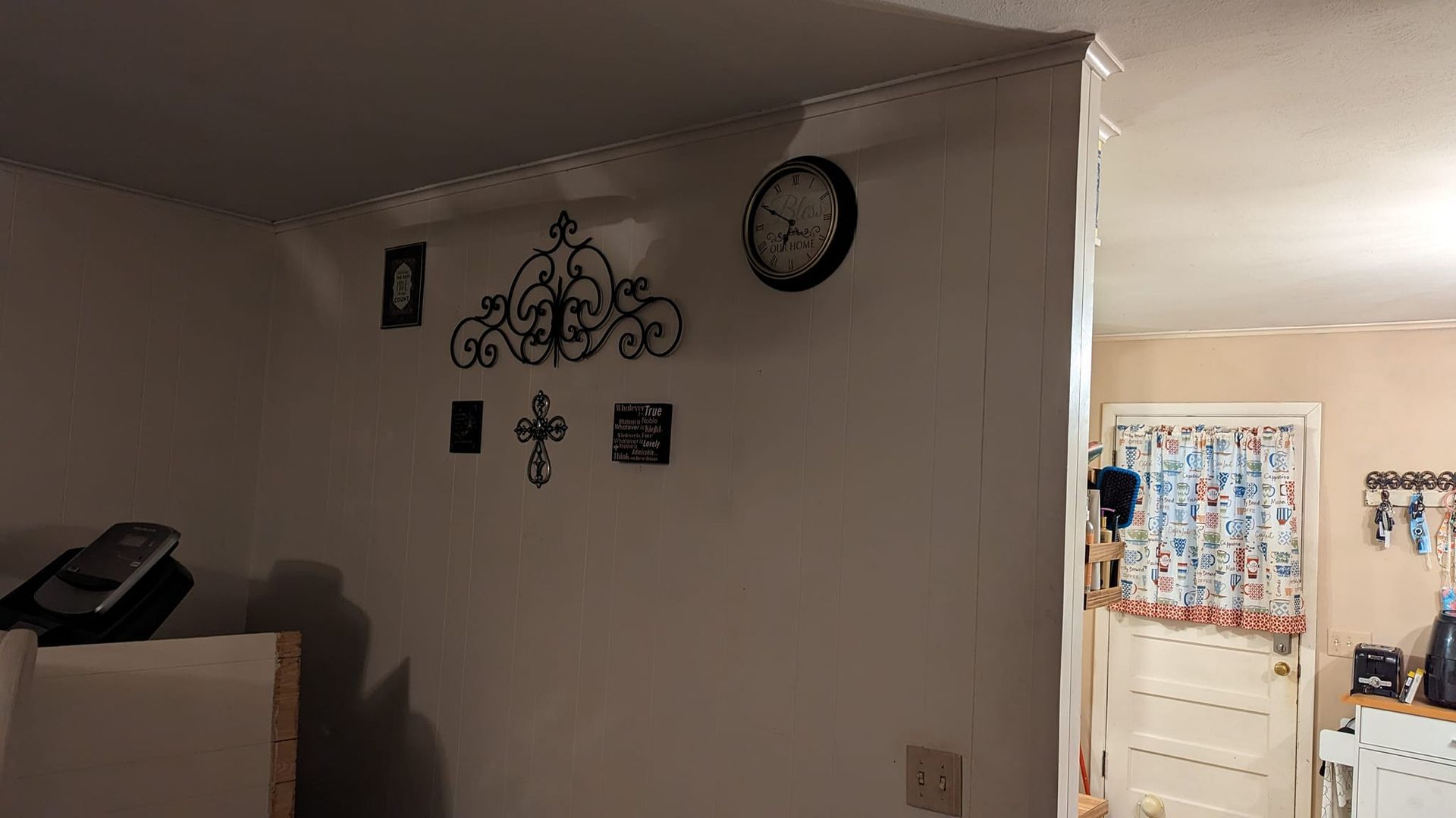 Off-white room with decorative wall art, a clock, and an open doorway.