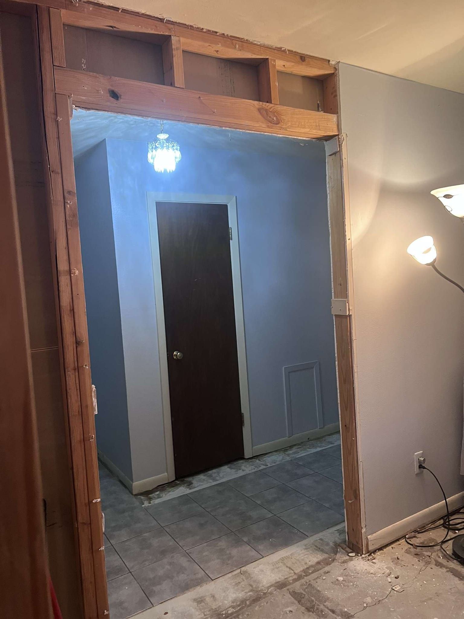 A doorway under construction reveals a hallway with a closed dark door. Gray walls and flooring.