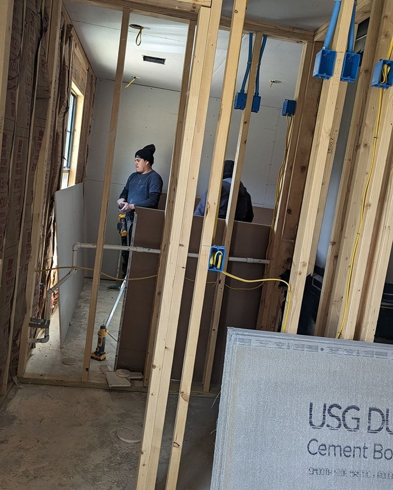 Person using a drill inside a room under construction. Wooden framing and drywall in progress.