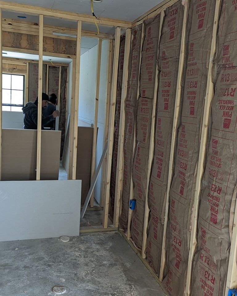 Interior view of a room under construction; wood framing, insulation, drywall, and a person working.