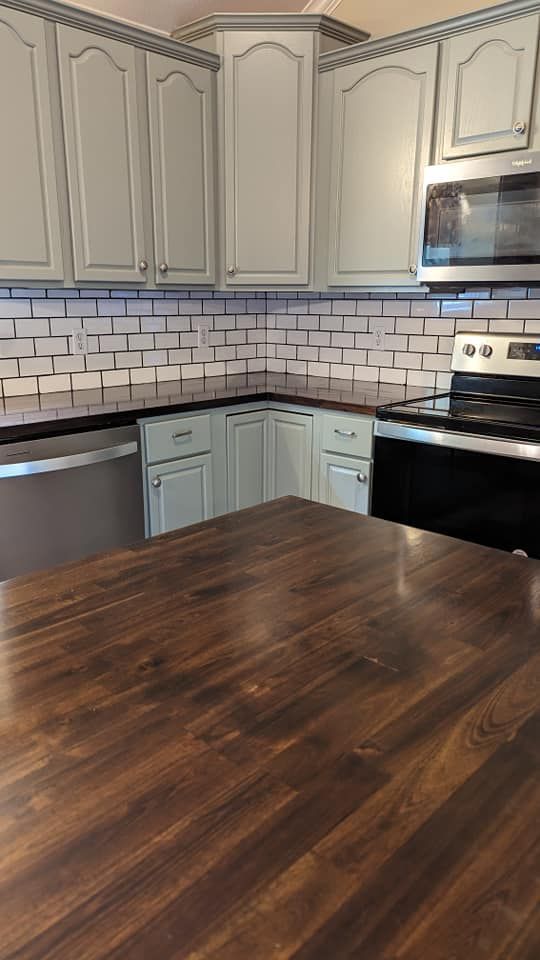 Kitchen with light gray cabinets, white brick backsplash, and dark wooden countertop island.