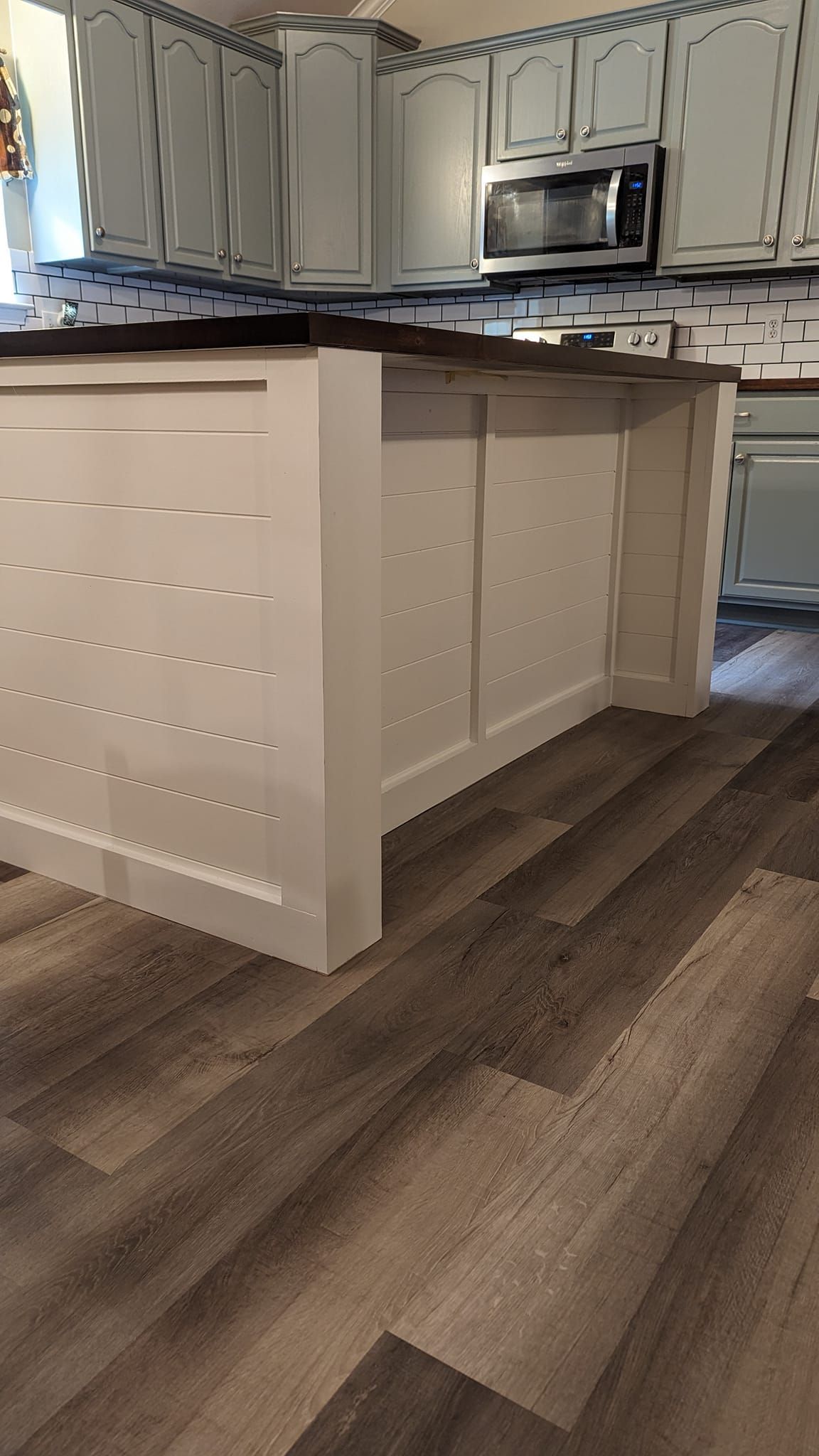 Kitchen with white cabinets, dark countertops, and a white island on wood-look flooring.