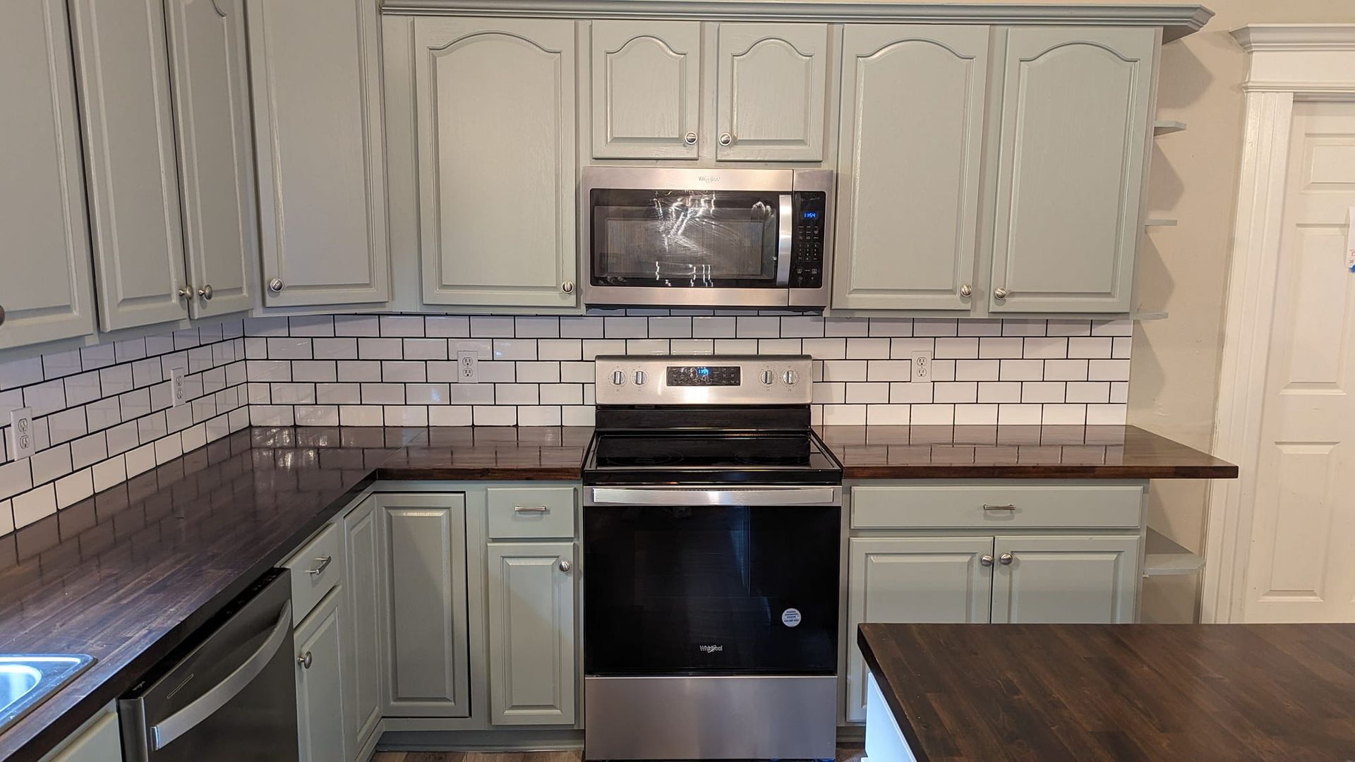 Kitchen with gray painted cabinets, stainless steel appliances, and dark wood countertops.