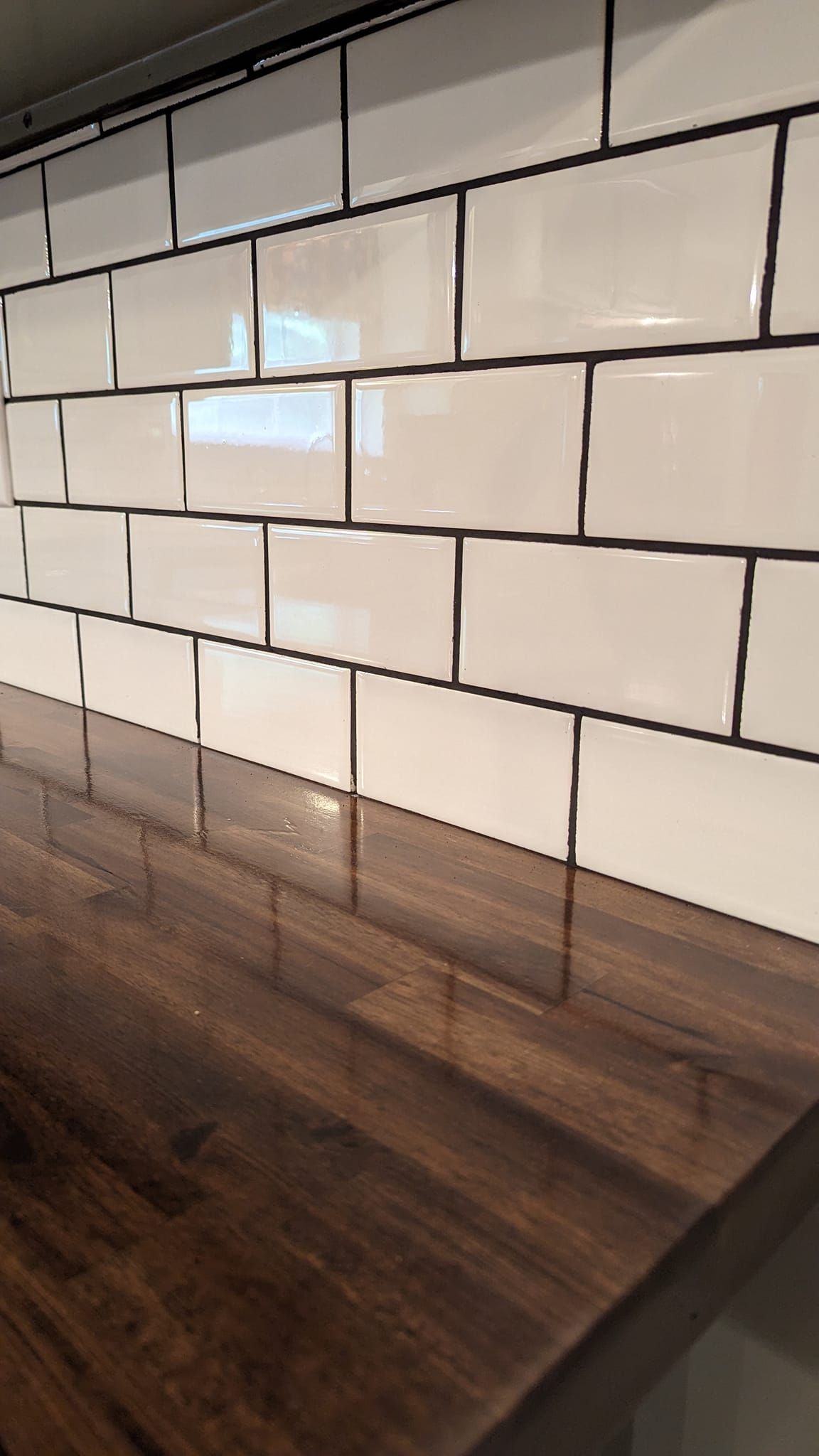 White subway tile backsplash with dark grout and a wood countertop.