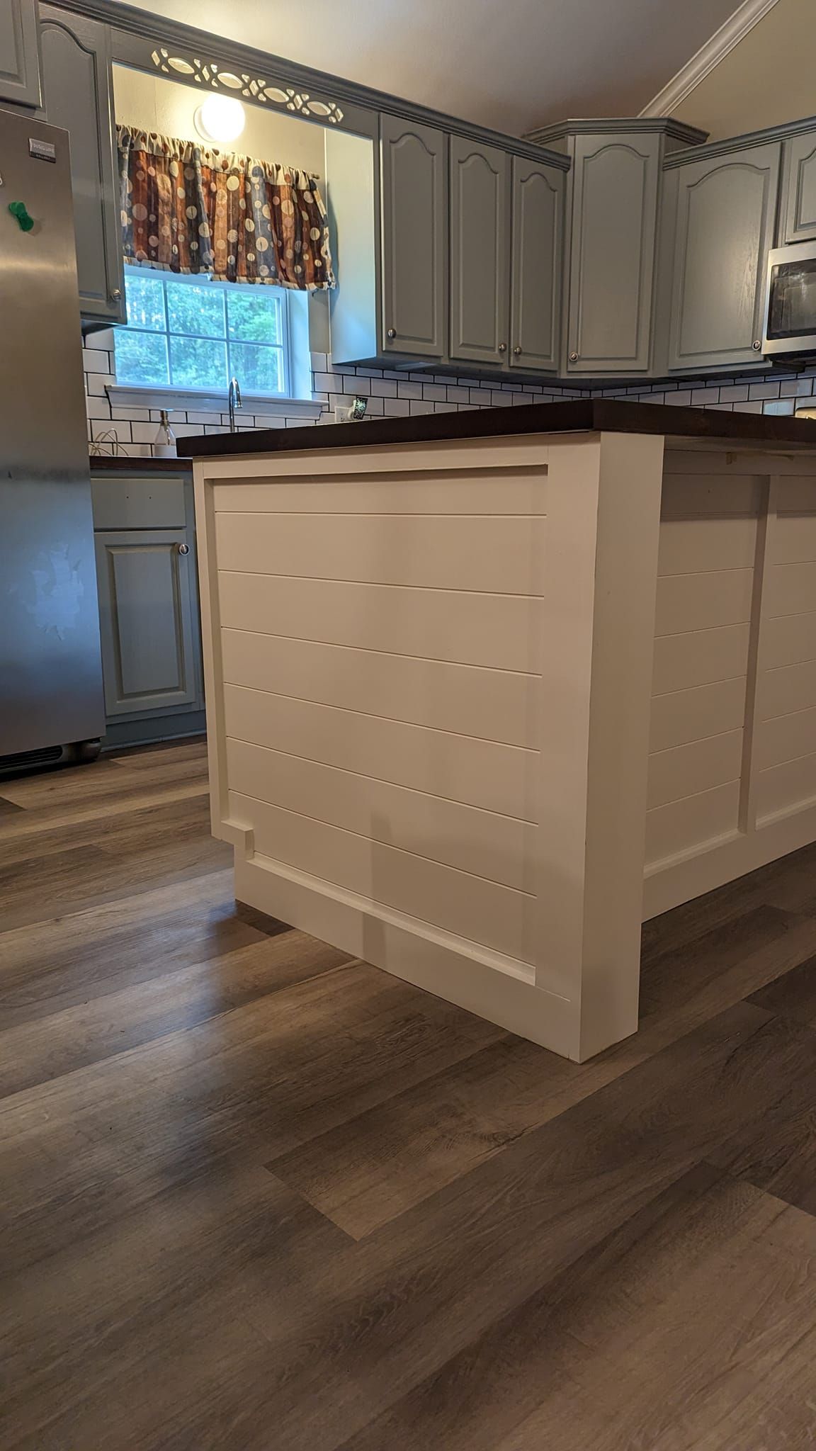 Kitchen with a light-colored island, cabinets, and wood-look flooring. A stainless steel refrigerator is visible.