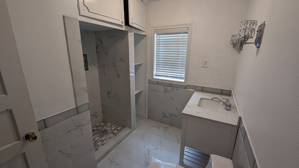 Bathroom with marble tile, a shower, vanity, and a window with blinds.