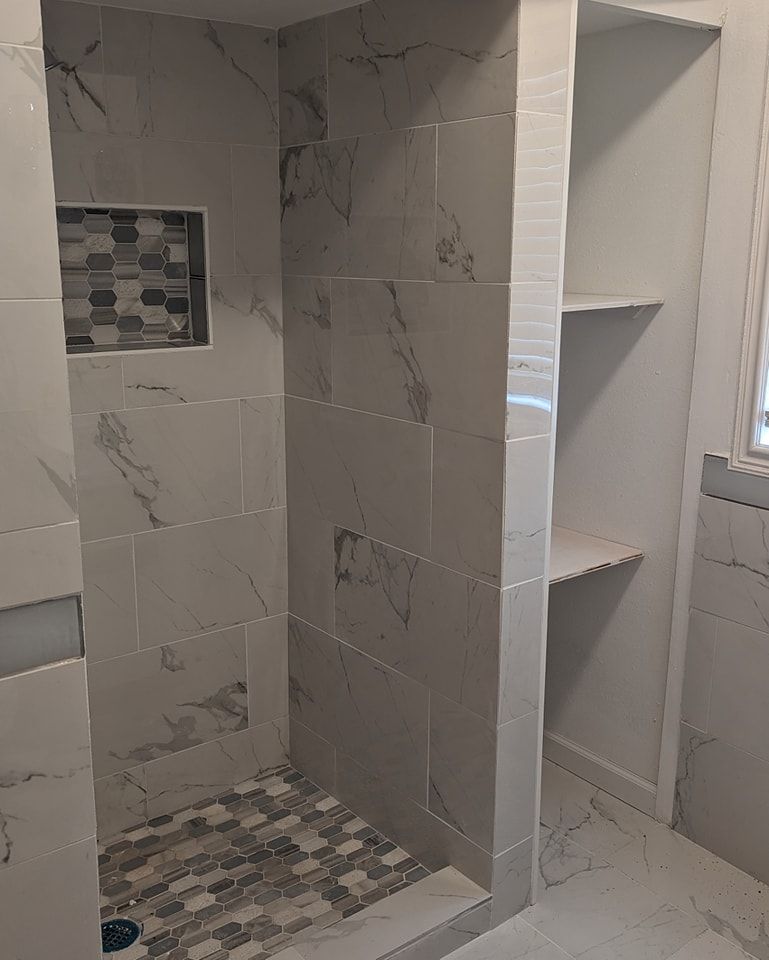 Tiled shower with marble-like walls and a mosaic floor. Built-in shelves on the right.