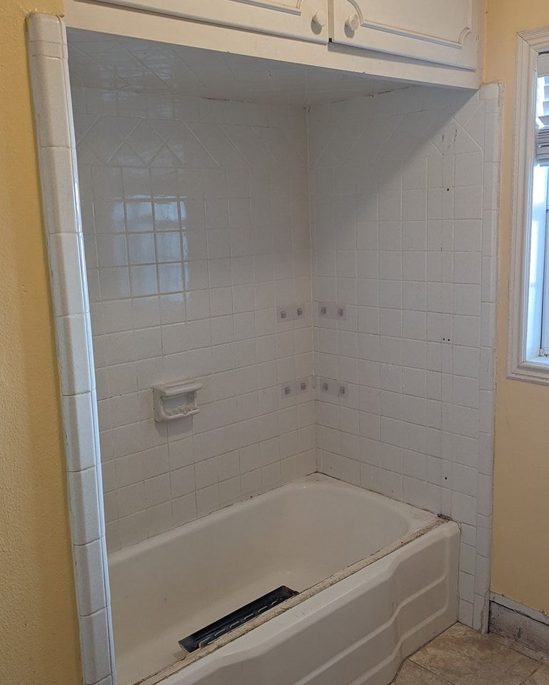 White tiled bathtub and shower enclosure with built-in cabinet.