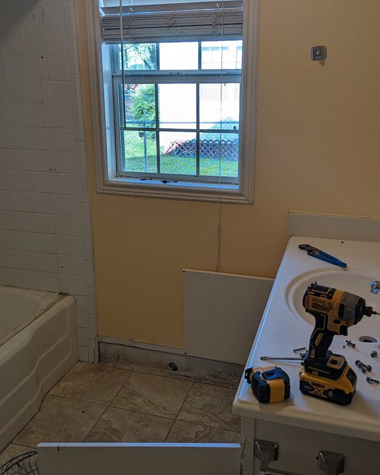 Bathroom renovation in progress. Yellow walls, window, vanity, tools, tile floor, and tub visible.