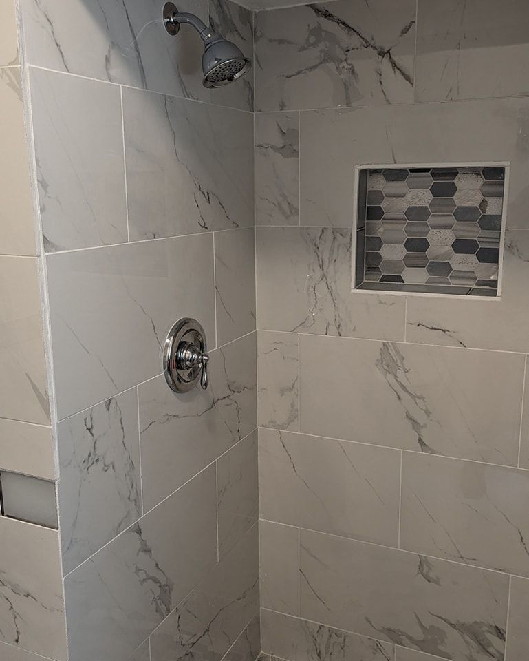 Shower with marble-patterned gray tiles, chrome fixtures, and a mosaic tile inset.