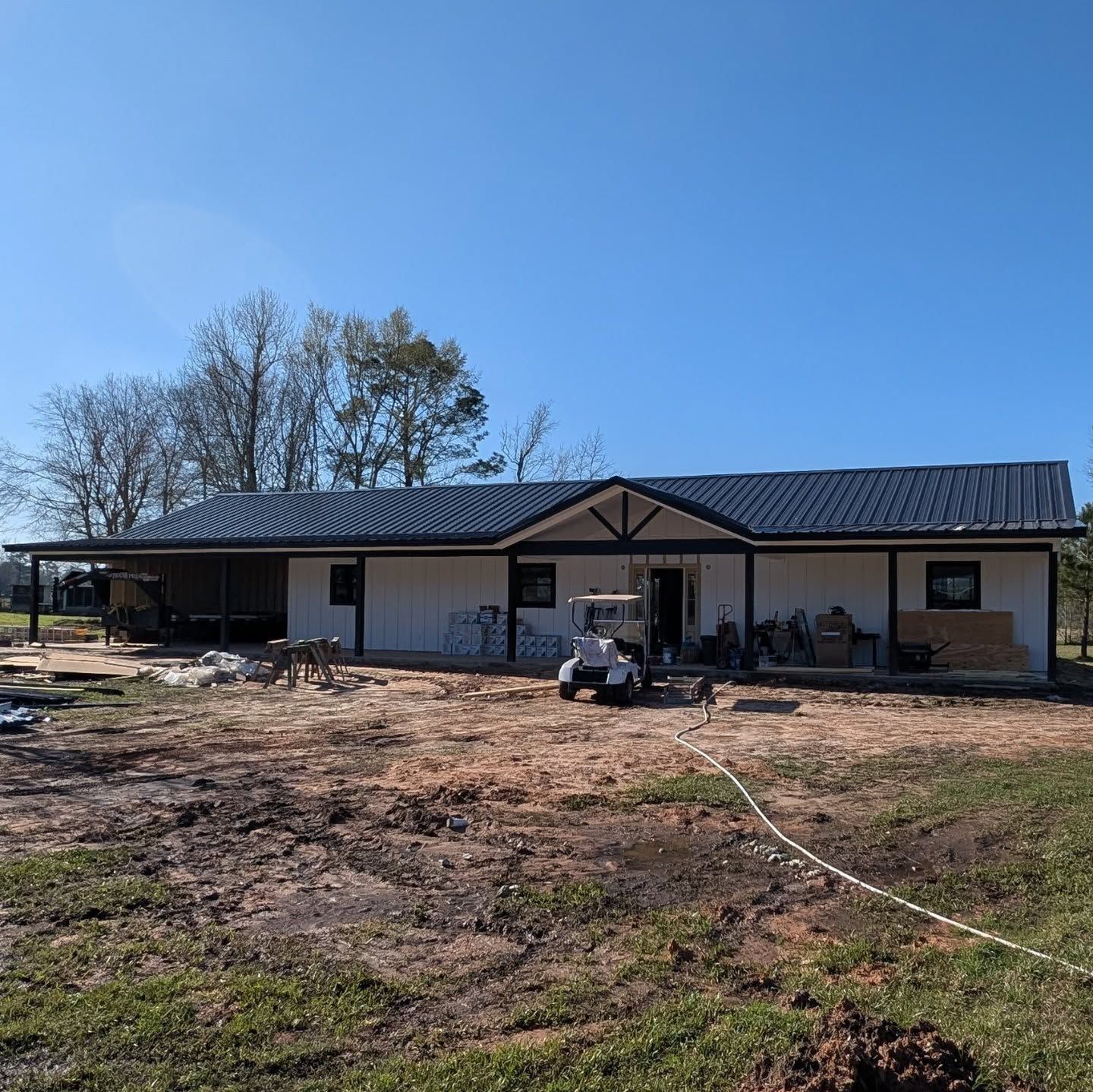 Exterior of a modern, white house with a dark metal roof, under construction on a sunny day.