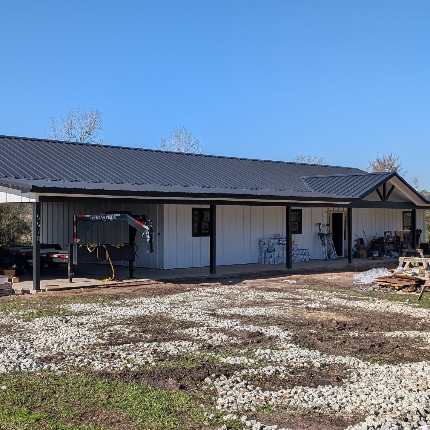 White house with black roof and trim; under construction, gravel yard, blue sky.