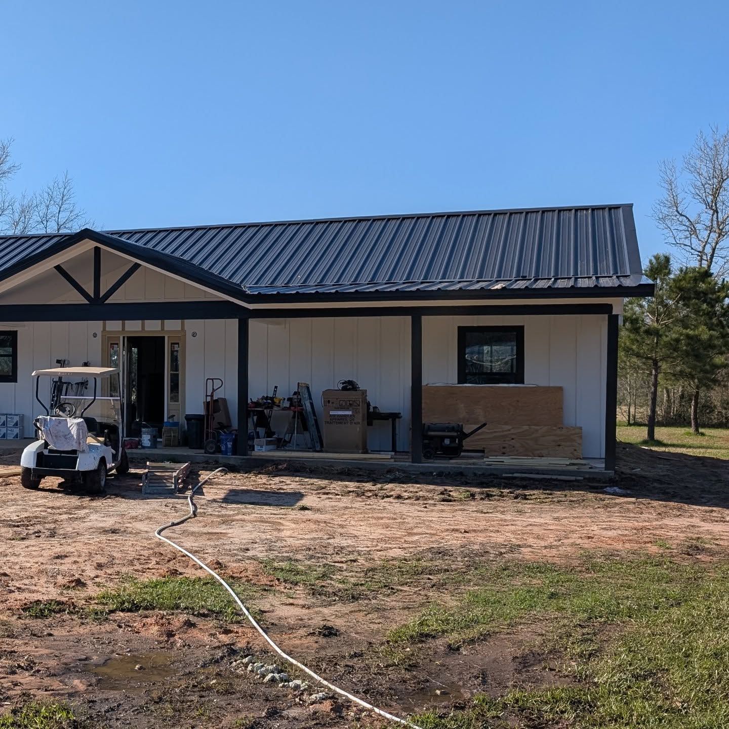 White house with a dark blue metal roof under construction; golf cart parked in front.