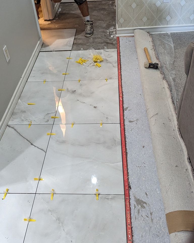 Installing floor tiles in a hallway. White tiles with leveling clips. Red level and rolled rug present.