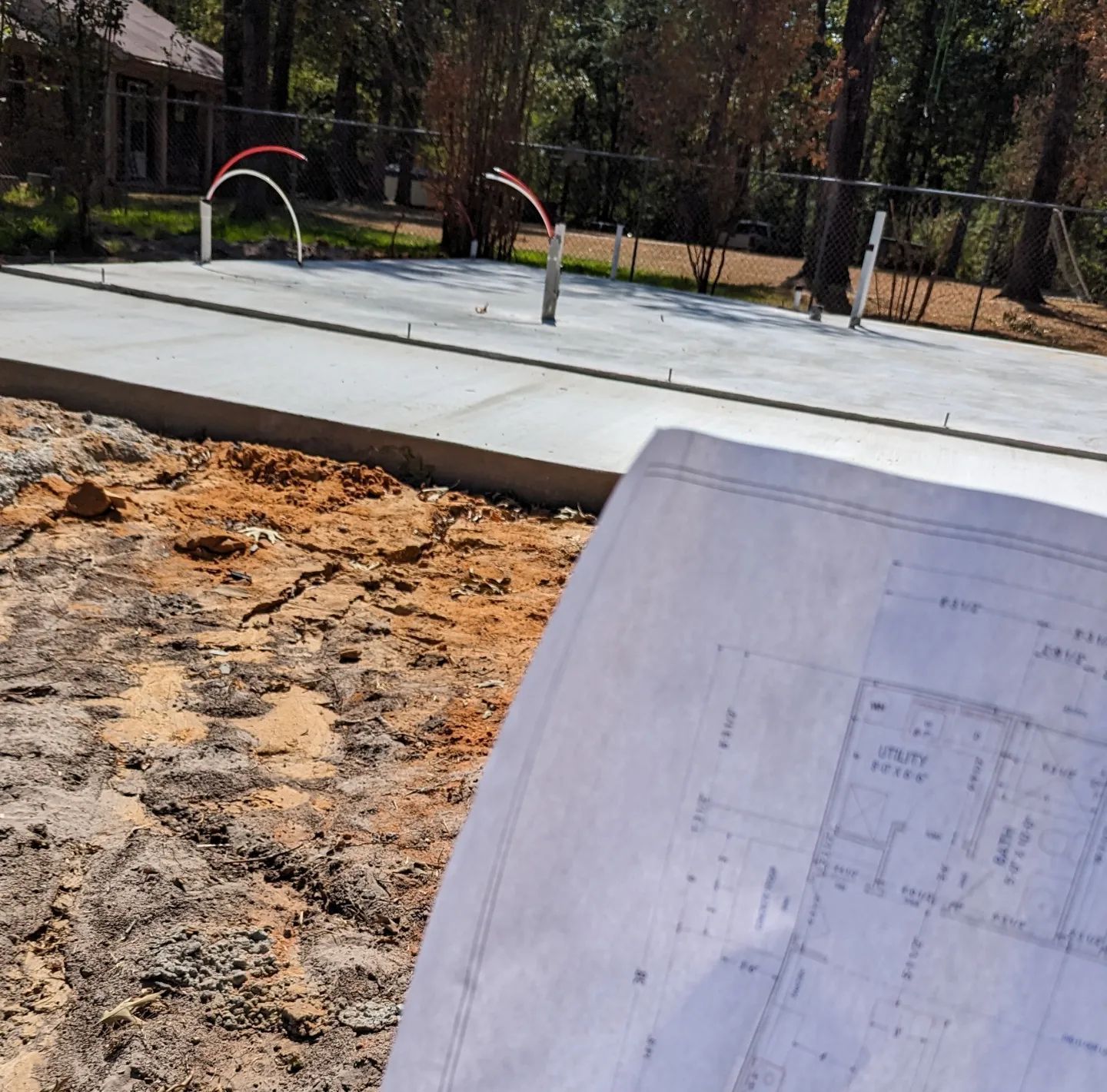 Construction site with a concrete foundation, plumbing pipes, and a blueprint.